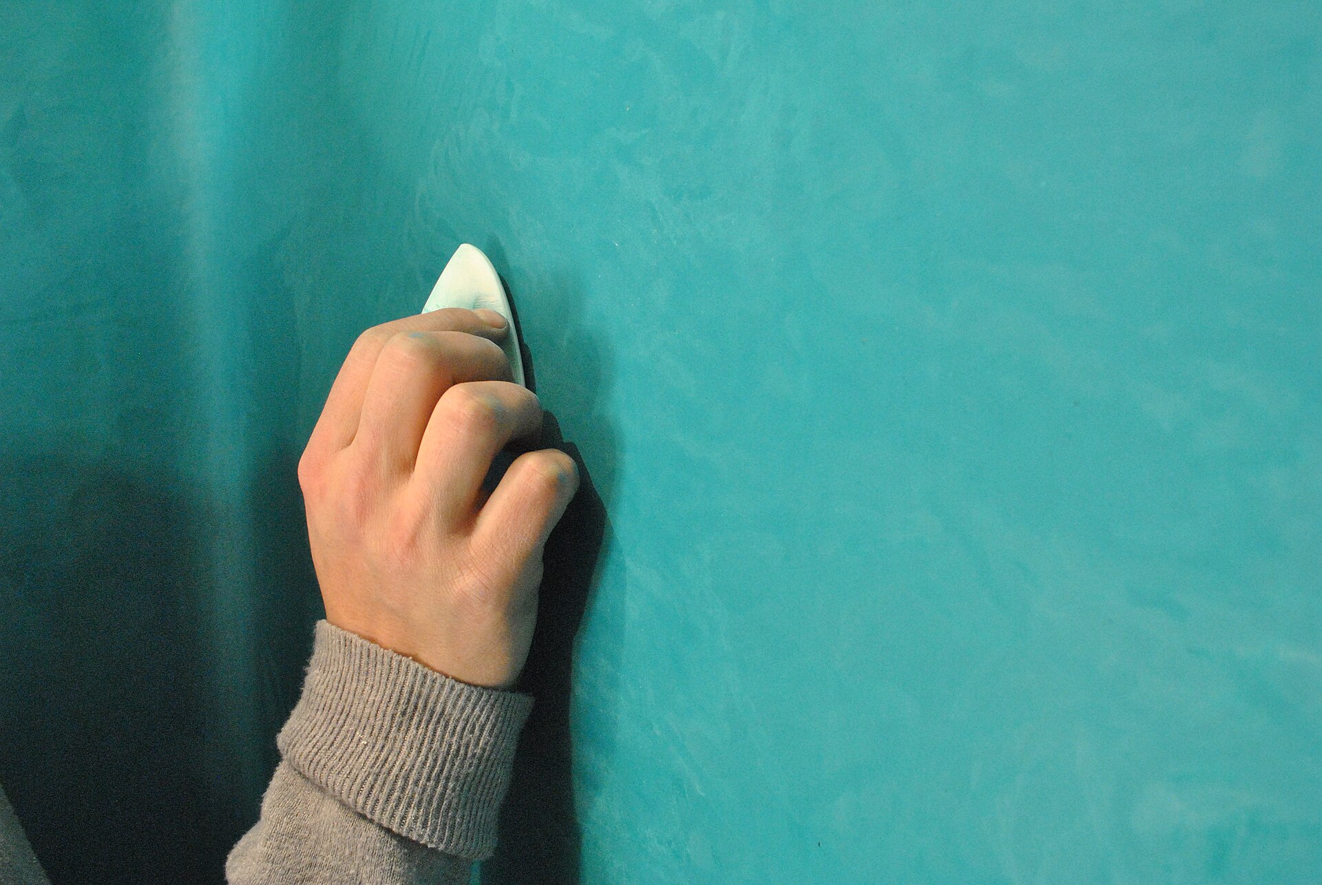 Main lustrant un enduit de chaux turquoise à la pierre